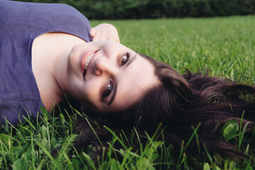 Obraz na płótnie Canvas Happy smiling caucasian young woman lying on grass. Copy space. Close-up outdoors portrait of plus size model with cute smile and beautiful hair spending time in nature. Summer recreation concept.