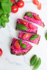 Fresh homemade beet root spread on a cutted slice of sourdought bread decorated with basil and tomato
