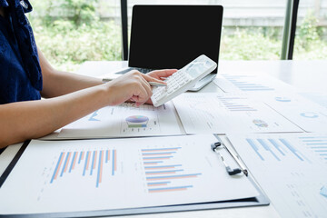 Office girl is sitting at a desk and use calculator calculating financial graph that show results In the office