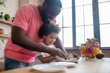 Tall dark-skinned man in a pink tshirt and his kid wiping the plate and feeling good