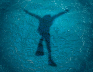 Scuba diver silhouette swimming under water in the ocean near the surface. Top vew