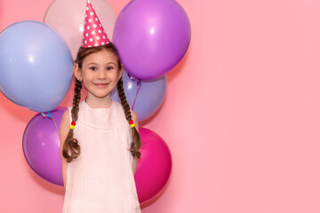 Happy little girl holds colorful balloons behind her back on a pink background. Holiday concept....