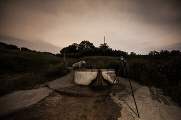 Photographic camera photographing a night landscape at a fountain in the field with stars.