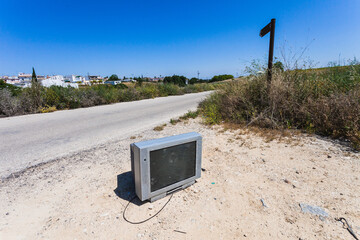 Old analog television lying in the field next to a road. Garbage and human waste in the environment. Pollution caused by humans.