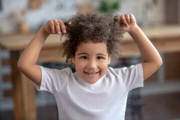 Cute curly-haired kid in a white tshirt looking naughty