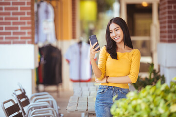 Asia woman walking and using a smart phone in the street in a sunny summer day