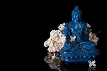 Blue Medicine Buddha framed by white lilac flowers on a black background with reflection