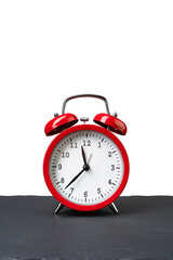 Vintage red alarm clock on dark slate plate isolated on white background. Copy space on the top. Vertical orientation.