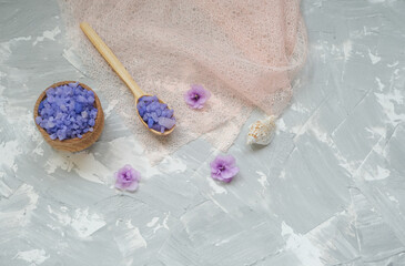 Bath salt in wooden bowl and in spoon. Violet flowers, purple sea salt on grey background..