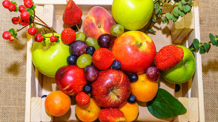 Set of berries and fruits in wooden box. Apple, strawberry, grape, berry and peach on a red brick background.