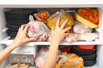 A woman takes out and puts frozen food in a freezer for long storage.