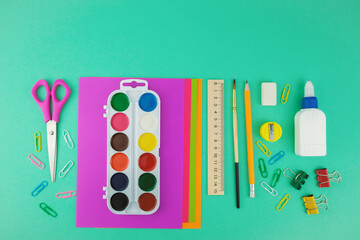 School supplies, top view of scissors, paper, watercolour paintings, brush, pen and ruler on the green background