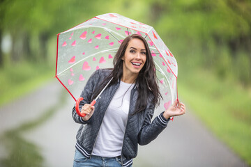 Beautiful brunette hides under the umbrella smiling at the camera on a rainy day
