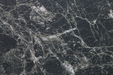 Texture of black marble with white lines of a pattern, macro background. Dark gray stone backdrop from mineral tile
