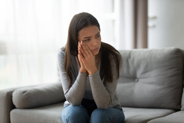 Thoughtful upset young woman sit on sofa feels disappointed frustrated, girl lost on thoughts thinking looks very unhappy, break up or divorce, hurt and jealous, broken heart, life troubles concept