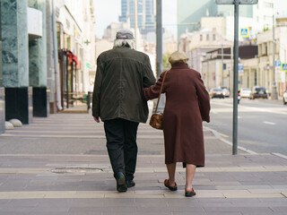 Photography of pair of aged man and woman. Backs / rear view. Pensioners go for a walk. Quarantine time is finished. Coronavirus pandemic lifestyle.