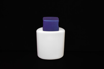 empty white vial from cosmetics with blue lid stands on a black background
