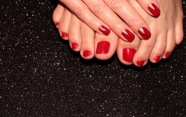 Red pedicure and manicure. A woman's leg and arm on a black background.