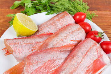 Raw headless gutted redfish carcasses, lemon and tomatoes close-up