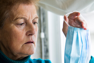 senior woman holding in her hand a medical mask to prevent viruses and infections