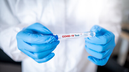 Medical scientist hand in personal protective equipment suit (PPE) wearing blue latex gloves holding COVID-19 Test tube in hospital laboratory. Male doctor getting result of Coronavirus case.