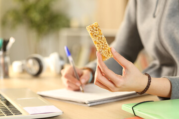 Student hands holding cereal snack bar studying