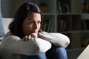 Pensive adult woman looking away thinking at night at home