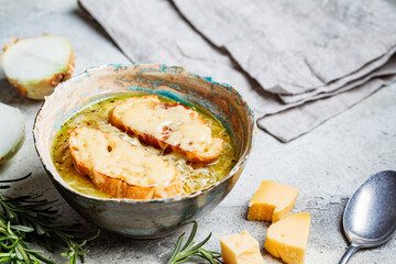 French traditional onion soup with baguette and cheese in gray ceramic bowl.