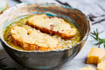 French traditional onion soup with baguette and cheese in gray ceramic bowl.