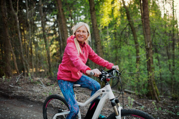Active senior woman with e-bike cycling outdoors in nature.