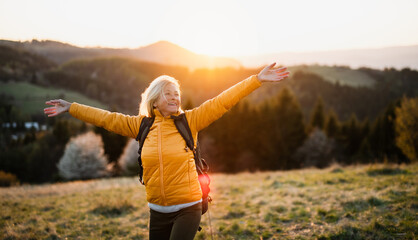 Front view of senior woman hiker standing outdoors in nature at sunset. - Powered by Adobe
