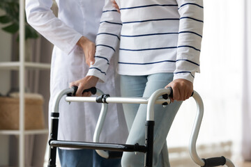 Cropped image caregiver helping to disabled patient walking with rollator equipment reduce load and...