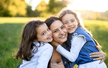 Mother with two small daughters having fun outdoors in spring nature, hugging.