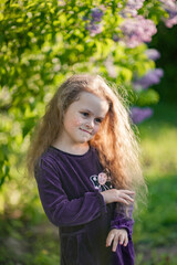 Outside portrait of a beautiful girl with long curly hair near lilac bushes