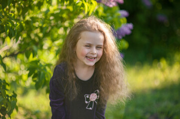Outside portrait of a beautiful girl with long curly hair near lilac bushes