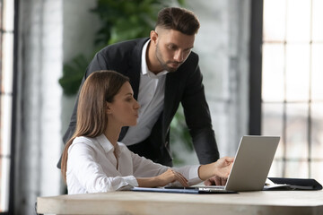 Businesswoman intern asking questions about online project to serious confident mentor, pointing at...