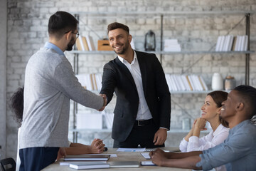 Smiling executive shaking successful employee hand at corporate meeting, thanking for good work...