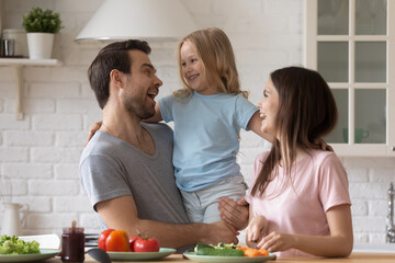 Overjoyed young family with small daughter have fun cooking together on modern kitchen, happy parents feel excited preparing breakfast healthy food with little girl child at home on weekend