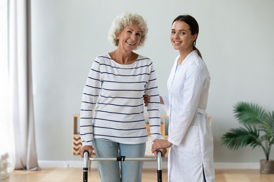 Elderly grandma holding walking frame feels satisfied after rehabilitation exercise therapy with female physical therapist, women smile look at camera. Caregiving, elder care and physiotherapy concept - Powered by Adobe