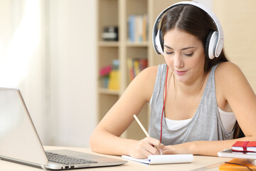 Naklejka premium Student with headphones taking notes at home