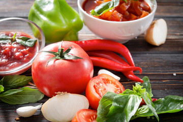 vegetable sauce, Lecho, ketchup with a sprig of green Basil, fresh tomato, red chili pepper, garlic, onion, sweet green pepper on a brown wooden