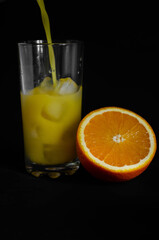 Fototapeta na wymiar glass of freshly squeezed orange juice with ice on black background