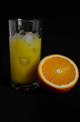 glass of freshly squeezed orange juice with ice on black background