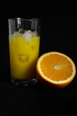 glass of freshly squeezed orange juice with ice on black background