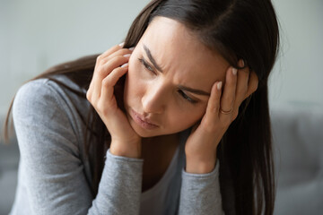 Close up face worried sad young woman sitting on couch looking away thinking about personal life...
