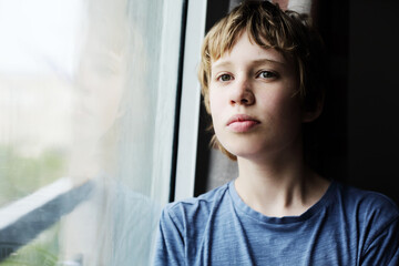 Cute 12 years old autistic boy looking through the window - 354259217