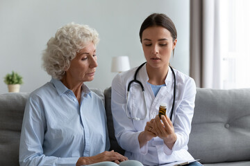 In living room young female caregiver practitioner nurse in white coat stethoscope on shoulders...