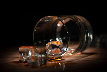 A glass of whisky with ice cubes on wooden background