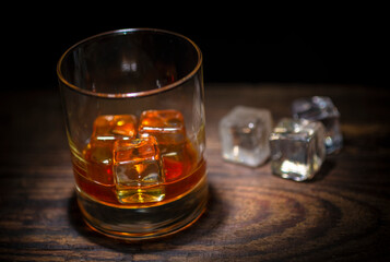 A glass of whisky with ice cubes on wooden background