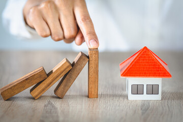Woman hand stopping risk the wooden blocks from falling on house, Investment risk and uncertainty in the real estate housing market, insurance.